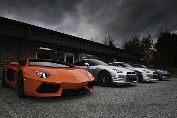 Lamborghini, Aventador, Nissan cars on the background of a building and a gray sky in clouds