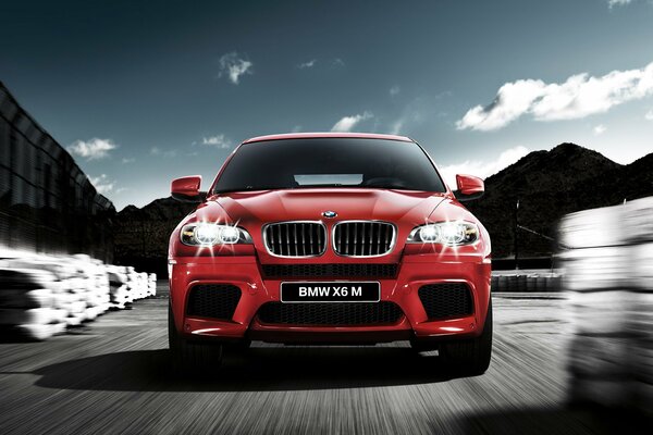 A red bmw x6 with its headlights on is flying down the road