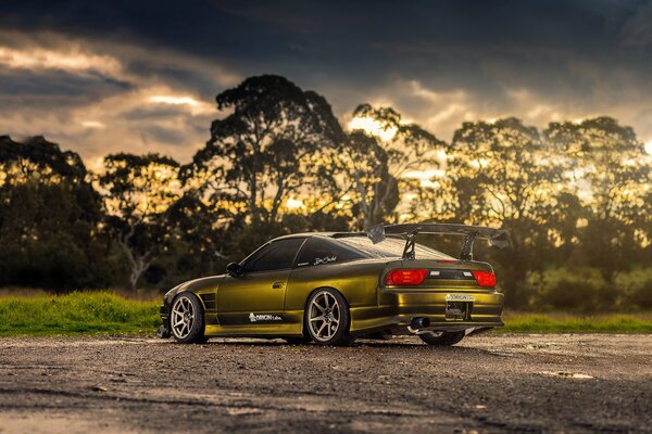 Green Nissan on the background of a cloudy sky with glimpses of the sun