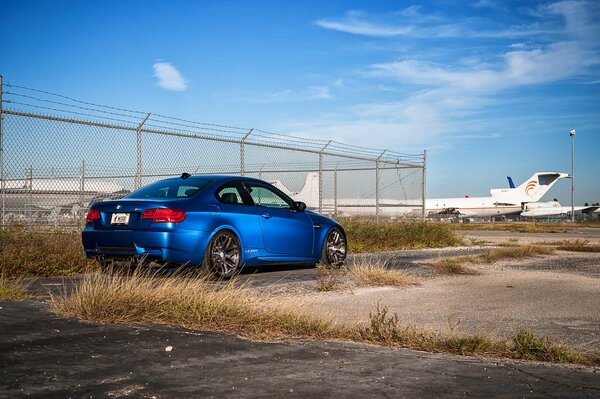 Blue BMW on the background of fencing and airplanes 