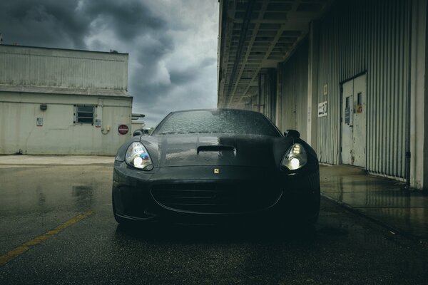 Ferrari negro, dividido por rayos de luz en el fondo de la zona industrial 