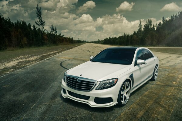 A road with a forest in the background and a white German car