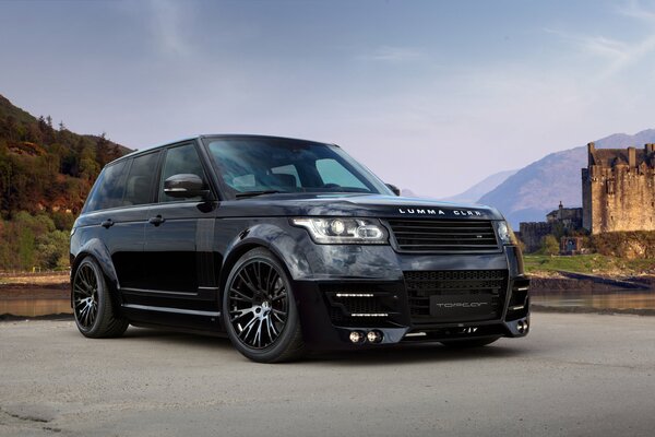 Range rover negro en el fondo de las montañas y el antiguo castillo