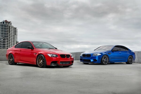 Deux voitures BMW rouge et bleu debout sur le toit d un bâtiment sur un fond de ciel nuageux