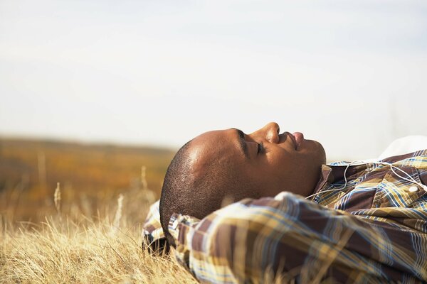 A bald dark-skinned guy is lying in a clearing