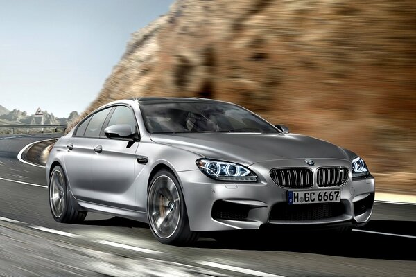 Машина bmw m6 gran coupe едет на скорости по холмистой местности