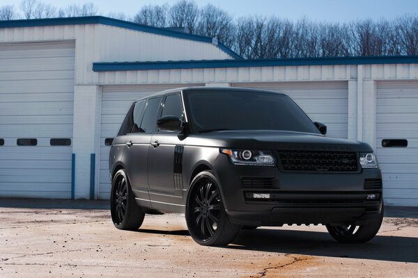 Un Land Rover noir mat avec des fenêtres teintées se trouve près des garages