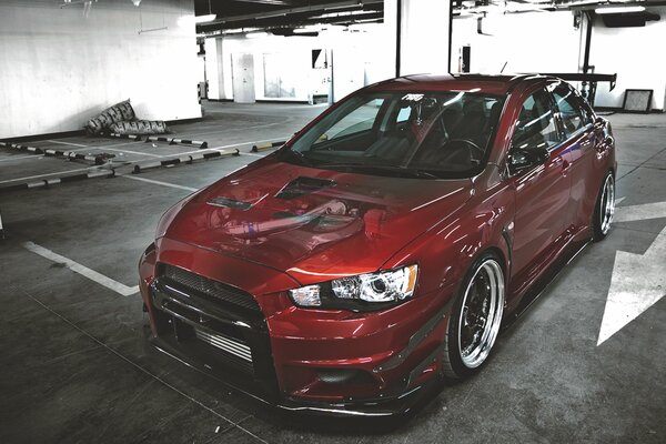 A red Mitsubishi Lancer car is parked in an underground parking lot