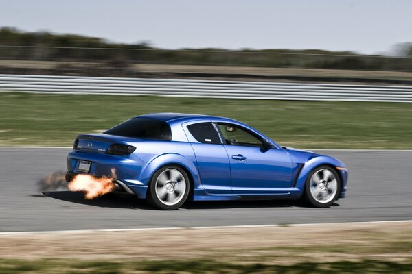 Auf der Strecke rast ein blauer Mazda mit Feuer aus dem Auspuff