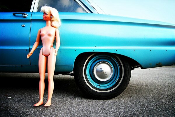 A doll leaning against the fender of a car