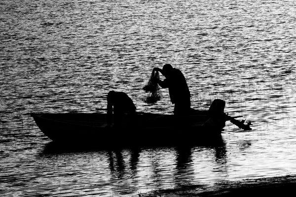 Fishermen on a boat collecting nets in black and white