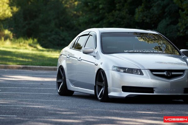 The acura tl white car stands near the trees