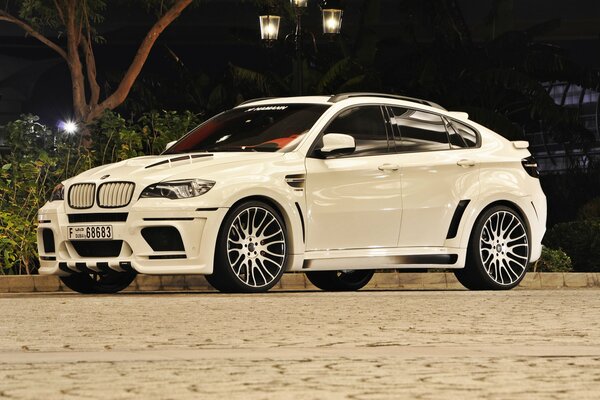 BMW blanco en la noche en la carretera en la iluminación de los fanaris