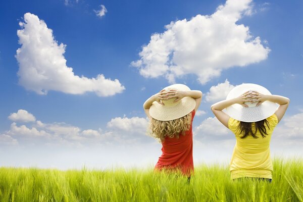Изображение двух девушек в шляпах в поле на фоне облачного неба