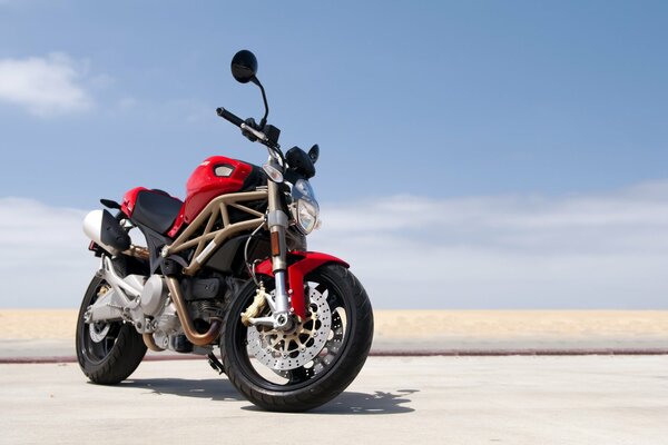 На пляже на фоне неба - красный спортивный мотоцикл