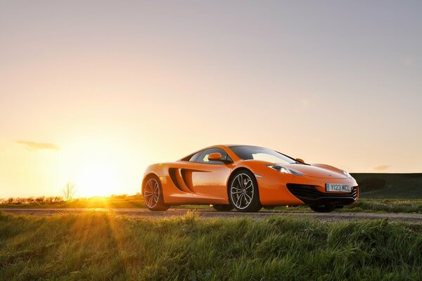 Fondo de pantalla con un McLaren mp4-12C naranja brillante contra el sol que se pone