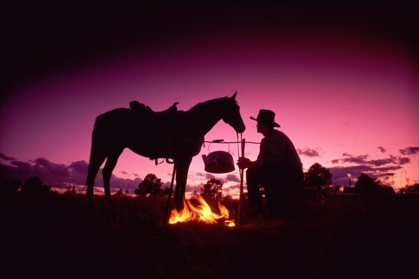 A cowboy and a horse lit a bonfire in the evening