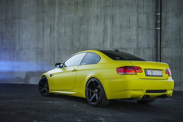 Yellow two-door car on the background of a concrete wall