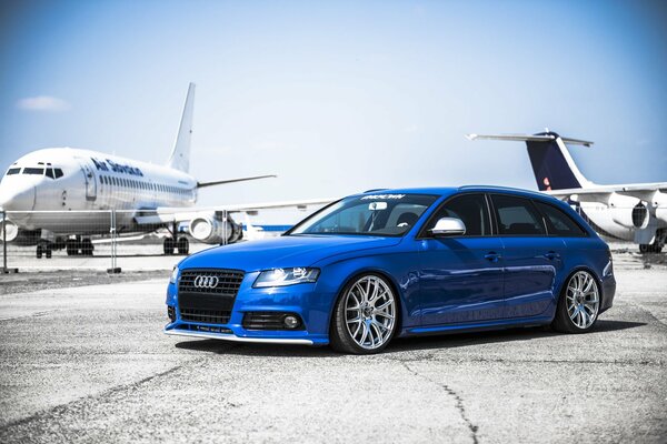 Blue audi a4 on the runway with airplanes