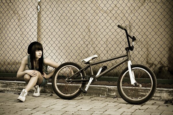 Ragazza con una bicicletta bmx lungo una recinzione a rete