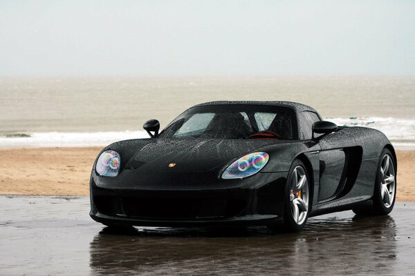 Porsche negro en la playa de la arena y el mar