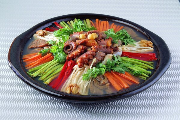 Octopus with vegetables on a black plate