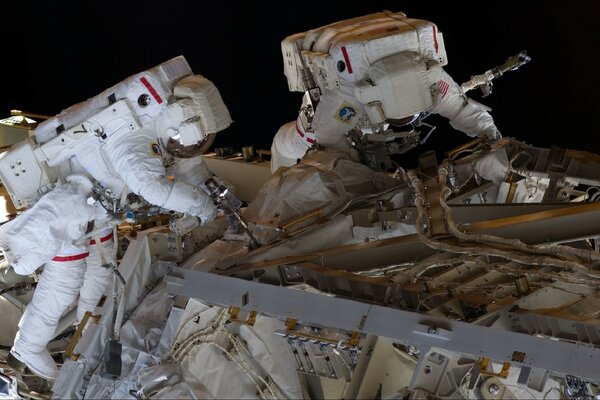 Astronauts repair equipment in outer space
