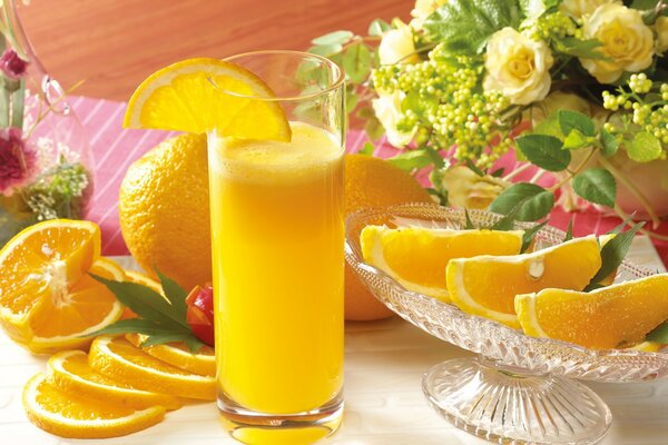 A glass of orange juice and orange slices in a vase