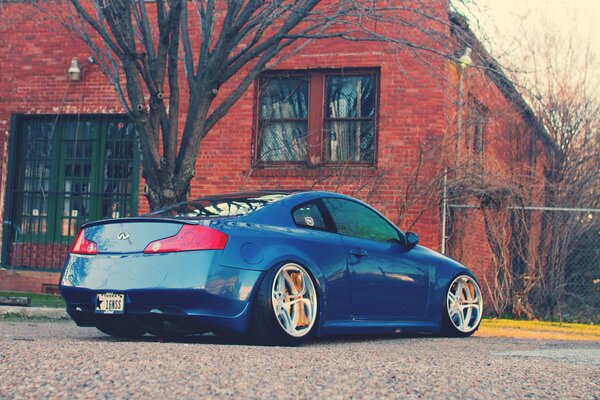 Blue Infiniti on asphalt on the background of a red brick house