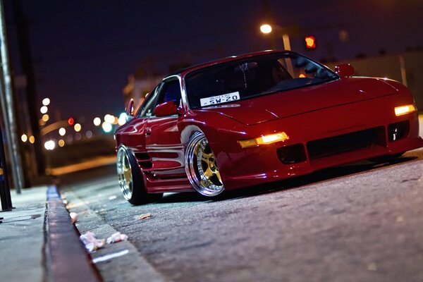 A red Toyota on a night road lit by lanterns