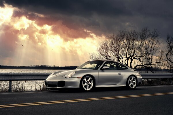 Silver Porsche se encuentra junto al agua bajo las nubes