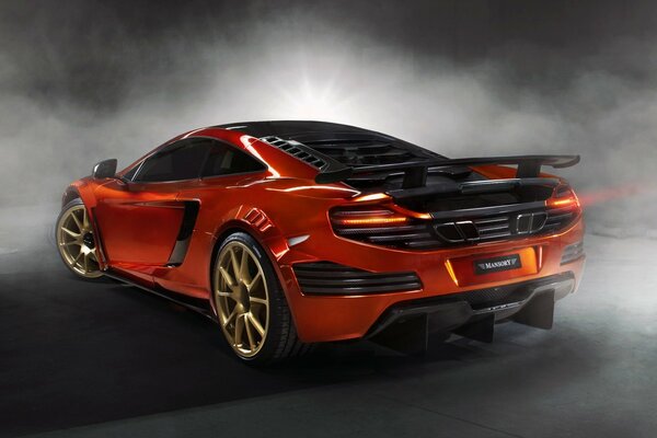 An orange McLaren stood against a background with a smoke effect