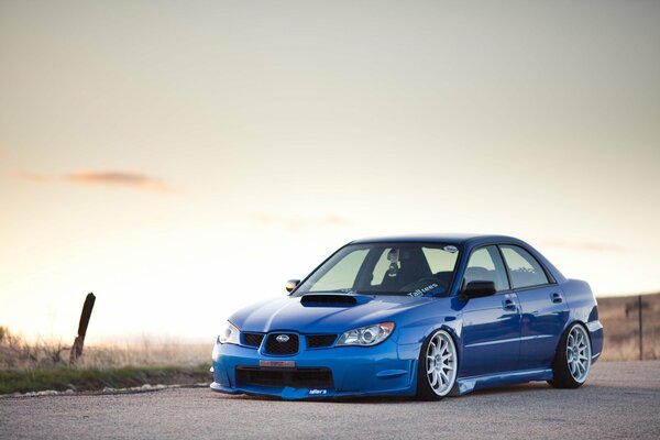 Azul Subaru zagorodom en el fondo del cielo despejado en la puesta del sol