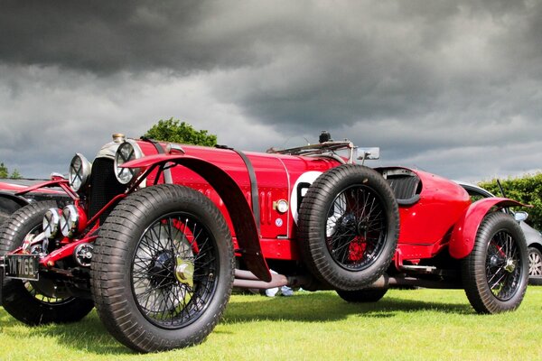 The red Bentley 3 car stands on the lush grass against the background of thick clouds