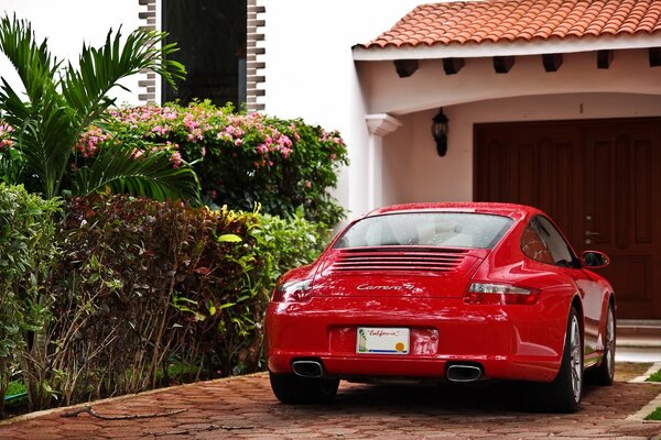 A red Porsche Carrera is parked near the garage