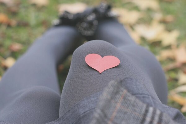 Linda foto de una chica con un corazón de papel en la rodilla