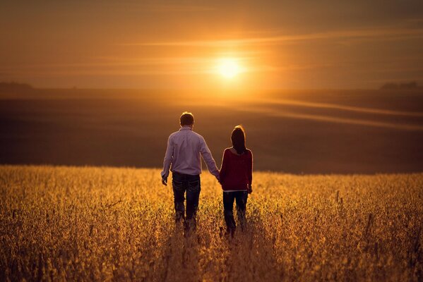 Pareja de enamorados caminando por el campo en medio de la puesta de sol
