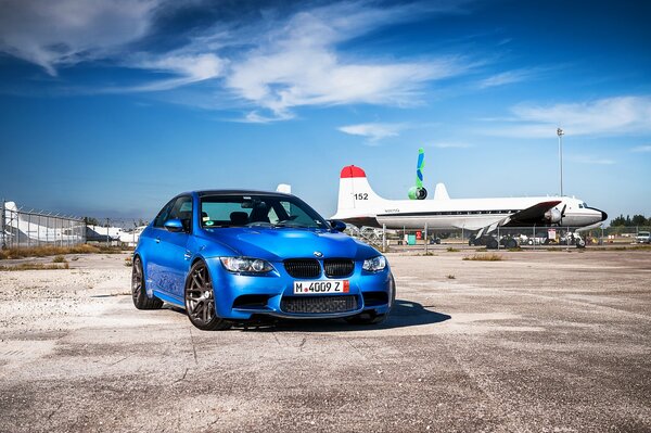 A blue BMW stands against the background of airplanes