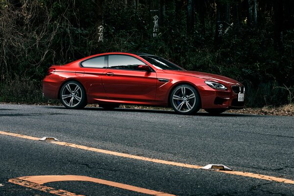 Red glossy BMW M6 coupe on the road in the shade