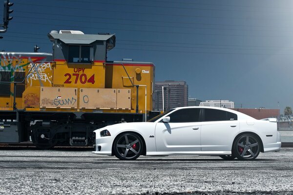 A tinted Dodge is standing near the train