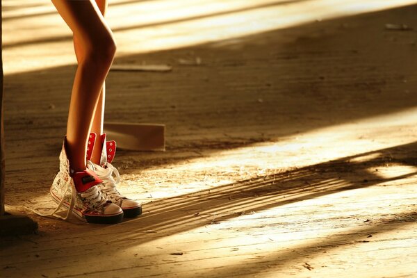 Piernas delgadas en Zapatillas de deporte en el Suelo de tablas