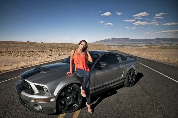 Bella ragazza in top arancione accanto a Mustang Ji Tee 500 nel deserto