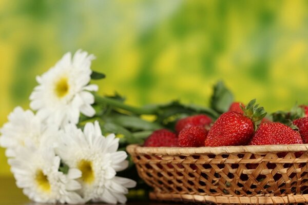 Erdbeeren im Korb. Nebenan ein Blumenstrauß aus Gänseblümchen