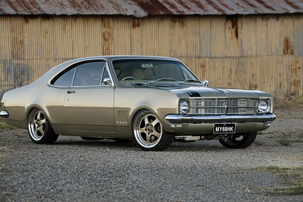 Retro beige car on asphalt against the background of an old metal shed