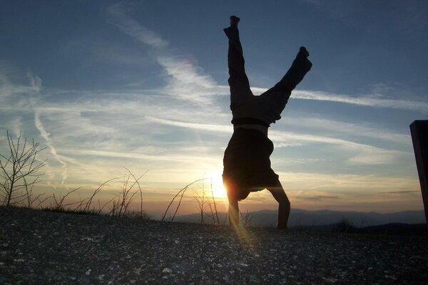 Sunset illuminates a man standing on his hands