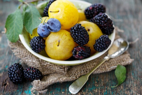 Berries, plums in a plate. Next to the spoon