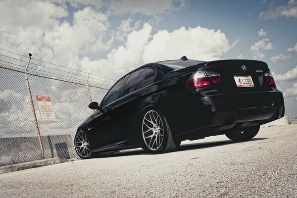 A black BMW car parked at a chain link fence on a small pebble