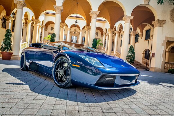 A blue glossy supercar near the colonnade of the palace