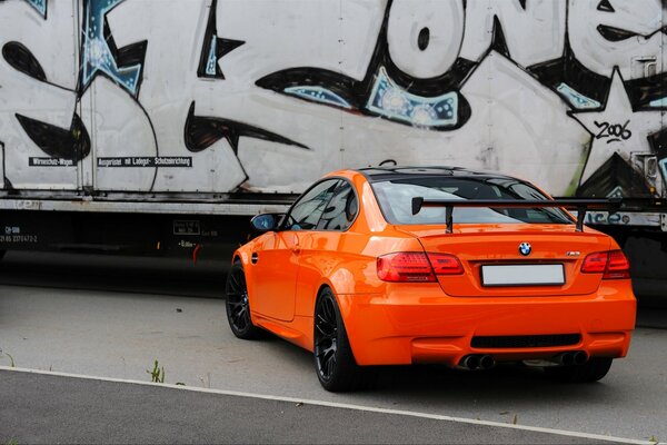 Pomarańczowe BMW coupe na tle ściany z graffiti