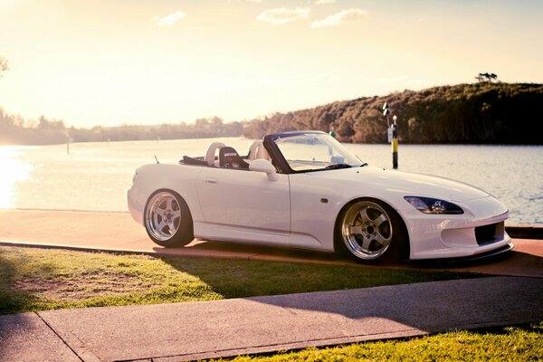 A white Honda with an open top rides along the embankment